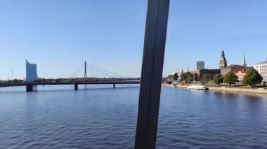 Riga şehir merkezi caddeleri köprüden tren penceresine bakıyor. Avrupa 'nın şehir mimarisini geziyorum. Baltık şehrinde güneşli bir günde büyük mavi nehir..