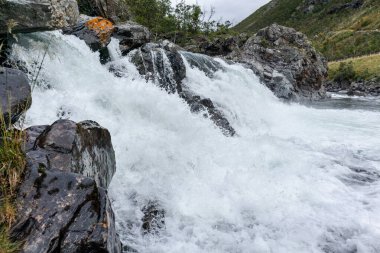 Su damlaları ve güzel dağ zeminli beyaz güçlü şelale makrosu. Doğa İskandinavya Norveç