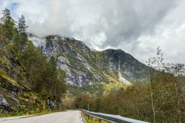 İskandinavya doğa yolculuğunda dağlar bulutlu bir yoldur. Sisli bulutlu gökyüzü ile kayalıklara ve orman tepelerine bakın. Kuzey manzarası sürüş yolu arka plan.