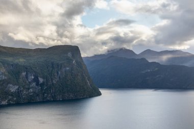 Soğuk gri renkli Norveç manzarası soğuk su yansıması ile fiyort kıyısında. İskandinavya 'da dramatik bir kuzey yazı. Kuzey arkaplanına git.