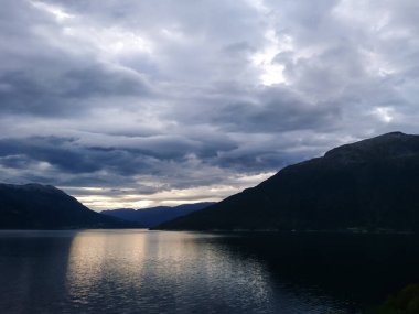 Günbatımı gökyüzünde ağır bulutlar ve Norveç 'teki dağlarda yansımalar. Norveç 'te akşam vakti koyu mavi