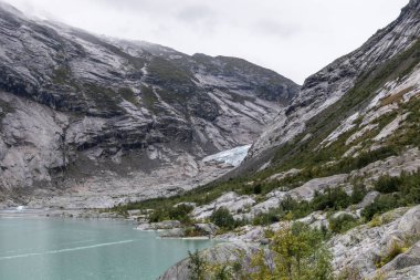 Norveç dağları göl kenarındaki mavi su, kayalar, buzullar, kar manzarası. Jostedalsbreen Ulusal Parkı 'ndaki Nigardsbreen' e bulutlu bir gezi.