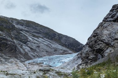 Jostedalsbreen Ulusal Parkı 'ndaki Nigardsbreen' e bulutlu bir gezi. Norveç dağlarının manzarası mavi buz, kaya, buzullar, kar. İklim değişikliği, eriyen buzullar