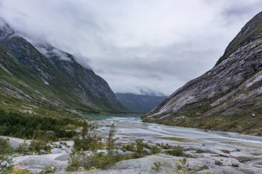 Norveç dağları, vadi manzarası, gök mavisi su, kayalar. Jostedalsbreen Ulusal Parkı 'ndaki Nigardsbreen' e bulutlu bir gezi.
