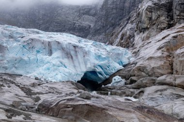 Jostedalsbreen Ulusal Parkı 'ndaki Nigardsbreen' e bulutlu bir gezi. Norveç dağlarının manzarası mavi buz, kaya, buzullar, kar. İklim değişikliği, eriyen buzullar