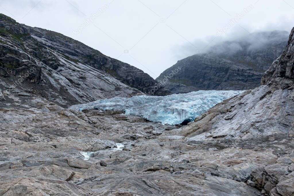 Cloudy day tracking trip to Nigardsbreen in Jostedalsbreen national park. Norway mountains landscape view with blue ice, rocks, glacier, snow. Climate change, melting glacier