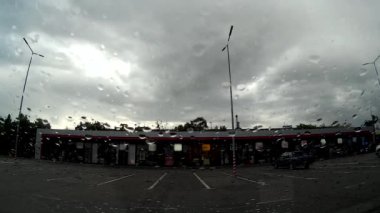 Yağmurlu zaman dilimi tam donanımlı video. Alışveriş merkezinin otoparkındaki yağmur damlaları arabanın ön camına düşer. Kasvetli bahar fırtınalı arka planı bulanık gri bir sahne