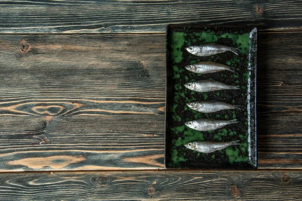 Small salted fish of Baltic herring, sprats on a wooden table. Top view. Concept — Stock Image Small salted fish of Baltic herring, sprats on a wooden table. Top view. Concept Stock Photo