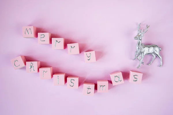 Merry christmas spelled out in wooden blocks. Pink color, silver letters and Christmas decoration silver deer
