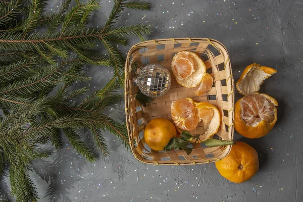 Новорічна композиція з мандаринами, очищеними мандаринами в кошику з різдвяними прикрасами та гілками ялинки. Вид зверху — стокове фото