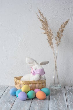Cezalı Paskalya. Sağlık maskeli Paskalya tavşanı ve renkli Paskalya yumurtaları. Dikey