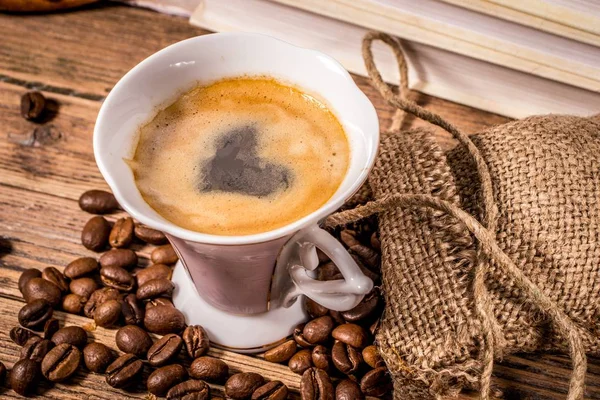 Cup of coffee with a heart painted in foam and grains scattered from a bag on a wooden table