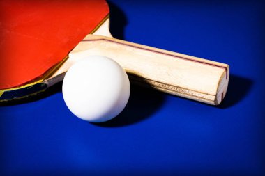 Masa tenisi için kırmızı raket ve top mavi masa arkasında.