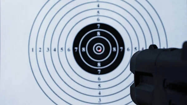 Background with a pistol aimed at a round target with a red dot from a laser sight in the center.