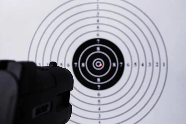 Background with a pistol aimed at a round target with a red dot from a laser sight in the center.