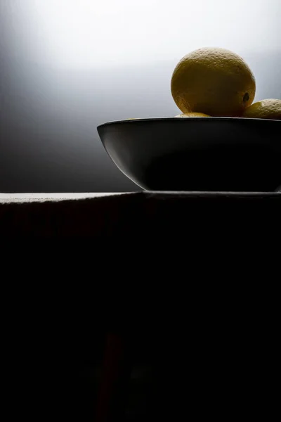 Yellow lemons in a black bowl, on a white wooden table