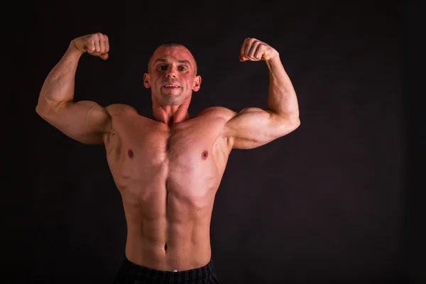 Beginnende bodybuilder poseren op een donkere achtergrond. — Stockfoto