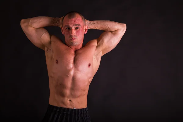 Beginnende bodybuilder poseren op een donkere achtergrond. — Stockfoto