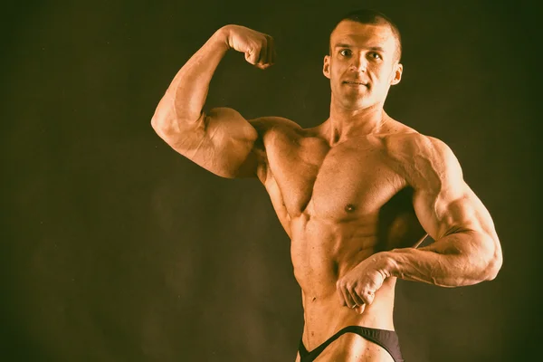 Bodybuilder poseren op een donkere achtergrond. — Stockfoto