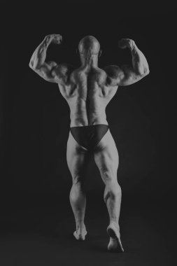 Siyah arka planda poz veren genç kaslı vücut geliştirici.