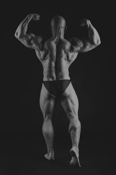 Young muscular bodybuilder posing over black background — Stock Photo, Image