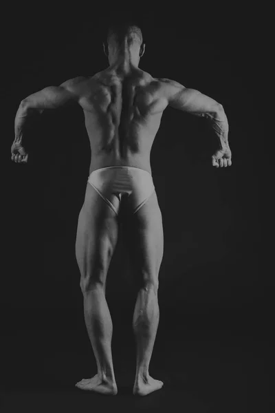 Young muscular bodybuilder posing over black background — Stock Photo, Image