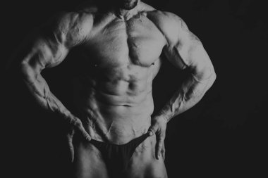 Siyah arka planda poz veren genç kaslı vücut geliştirici.