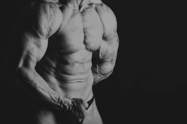 Siyah arka planda poz veren genç kaslı vücut geliştirici.