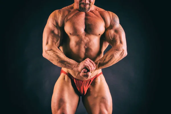 Bodybuilder posing in different poses demonstrating their muscles. Failure on a dark background. Male showing muscles straining. Beautiful muscular body athlete.