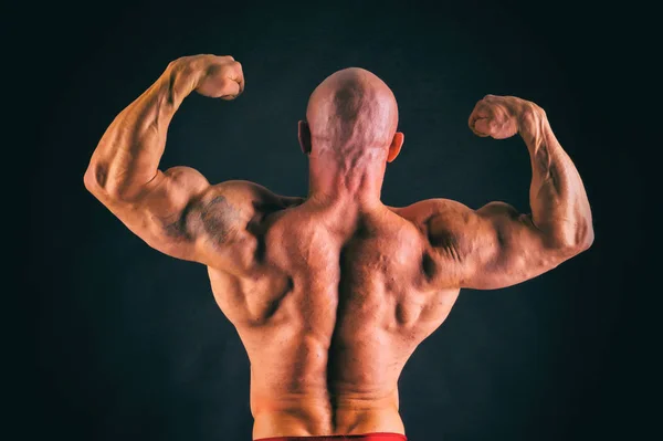 Fisiculturista posando em diferentes poses demonstrando seus músculos. Falha num fundo escuro. Homem mostrando músculos se esforçando. Bonito atleta corpo muscular . — Fotografia de Stock