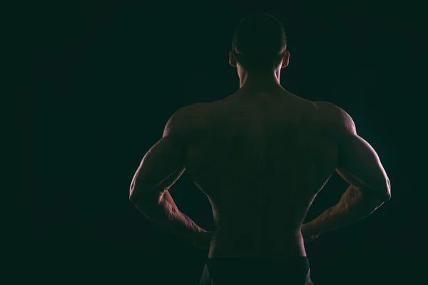Silhouette vackra bodybuilder på en mörk bakgrund. — Stockfoto