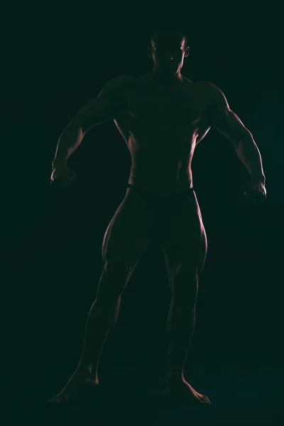 Silhouette schöner Bodybuilder auf dunklem Hintergrund. — Stockfoto