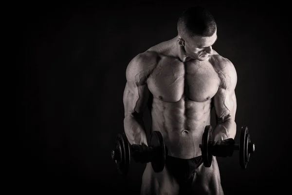 Um homem com um corpo muscular lindo em um fundo preto — Fotografia de Stock