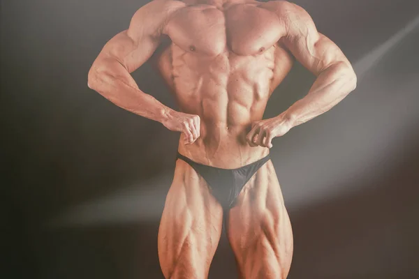 Um homem com um corpo muscular lindo em um fundo preto — Fotografia de Stock