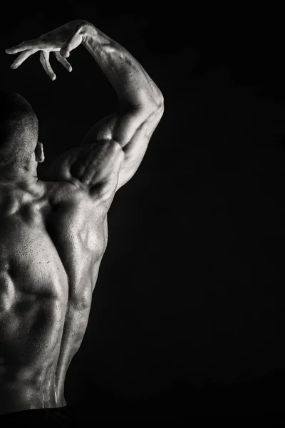 Um homem com um corpo muscular lindo em um fundo preto — Fotografia de Stock