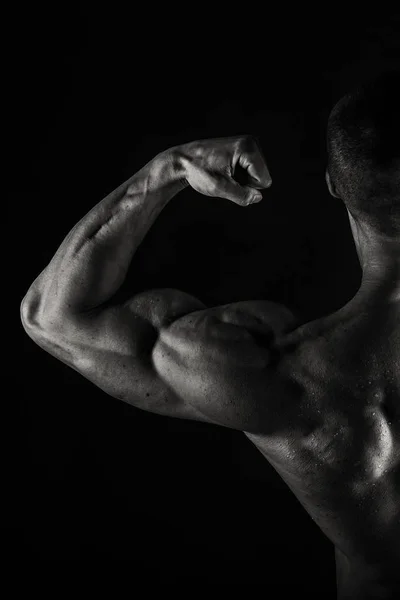 Um homem com um corpo muscular lindo em um fundo preto — Fotografia de Stock