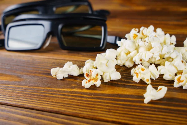 Popcorn sciolti e occhiali 3D su uno sfondo di legno — Foto Stock