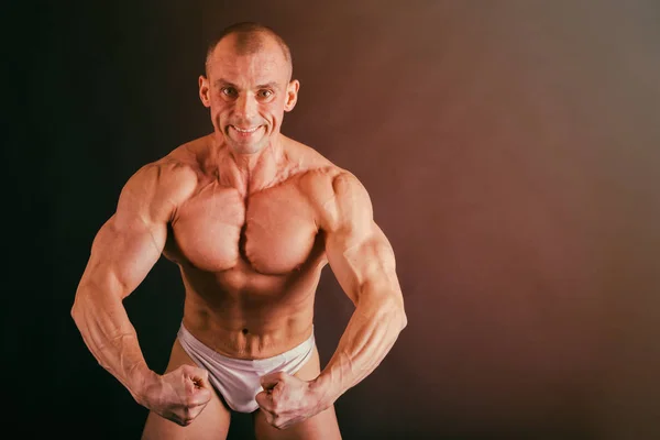 Culturista posando en diferentes poses demostrando sus músculos. Fracaso en un fondo oscuro. Varón mostrando tensión muscular. Hermoso atleta cuerpo muscular . — Foto de Stock