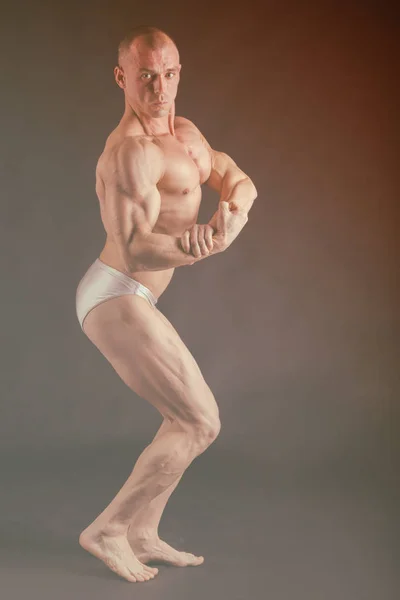 在不同的姿势，展示他们的肌肉构成的健美运动员。一个黑色的背景上的失败。男性显示肌劳损。美丽的肌肉发达的身体运动员. — 图库照片