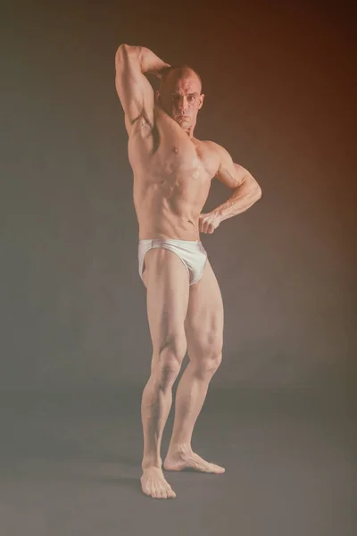 ボディービルダーの筋肉を示すさまざまなポーズでポーズをとるします。暗い背景上に失敗しました。男性を示す筋肉に負担をかけます。美しい筋肉体アスリート. — ストック写真