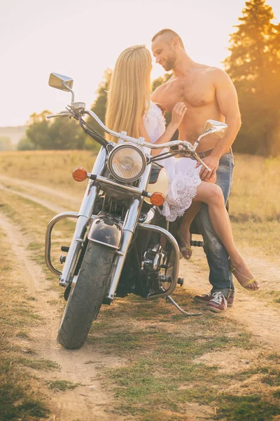 Casal amoroso em uma motocicleta em um campo — Fotografia de Stock