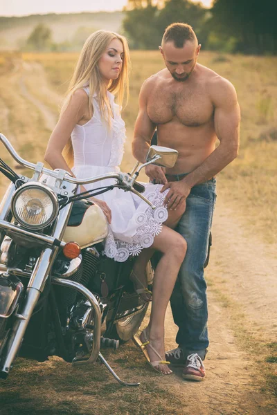 Casal amoroso em uma motocicleta em um campo — Fotografia de Stock