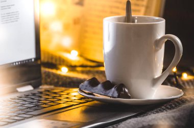 Parlak Noel ışıklarının arka planında çikolata olan bir fincan sıcak çay. Yeni yılın sıcak ve samimi atmosferi.