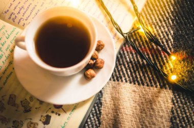 Noel ışıkları ve bir fincan sıcak çay, rahat bir battaniye ve defter, kış atmosferi.