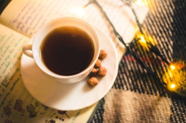 Noel ışıkları ve bir fincan sıcak çay, rahat bir battaniye ve defter, kış atmosferi.