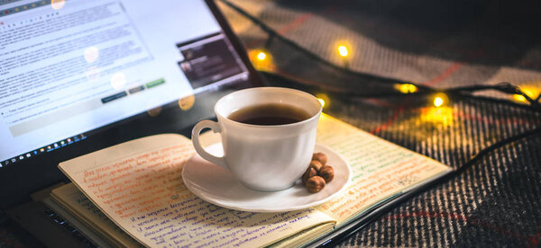 Чашка горячего чая в рождественской атмосфере с ноутбуком, уютным одеялом и книгой в теплых тонах
