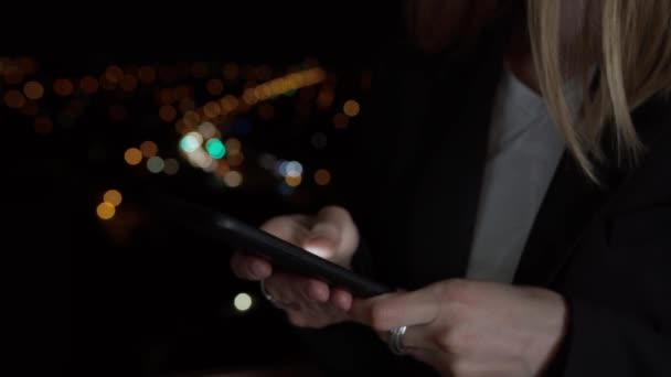 Gros plan défocaliser les mains de la femme en utilisant le téléphone mobile sur fond de belles lumières de la ville de nuit. Style de vie des jeunes gens élégants avec téléphone intelligent. Navigation sur le site, défilement 