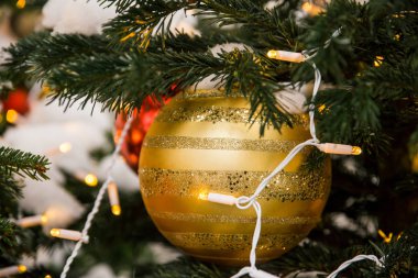 Altın çizgili Noel balosu, pullar ve çelenkler Noel ağacında. Arka planda bulanıklık var.