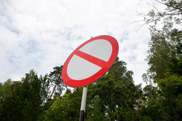 Round red crossed-out empty sign on a black-and-white pole close-up in the middle of the forest and sky