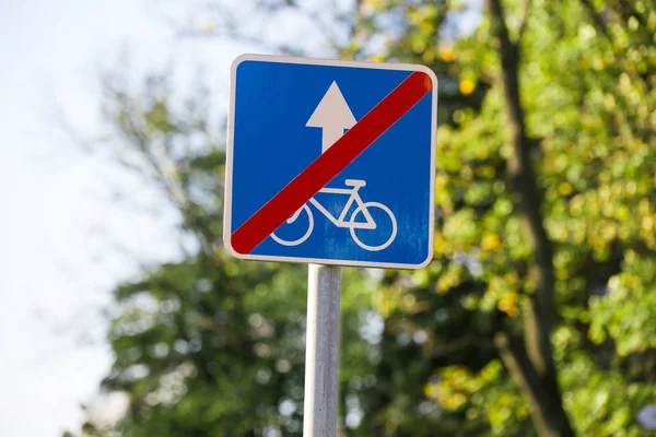Niebieski czerwony kwadrat przekreślony znak drogowy Koniec pasa dla rowerzystów zbliżenie na rozmazanym tle nieba, drzewa — Zdjęcie stockowe
